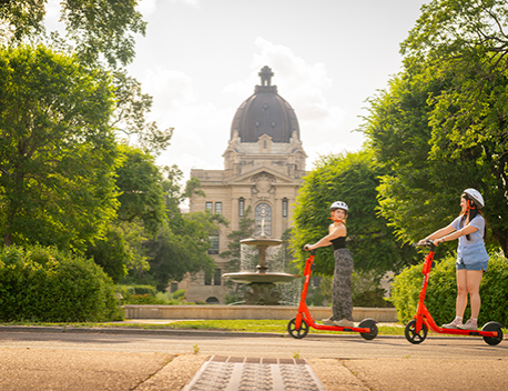two girls riding electric scooters at a park.